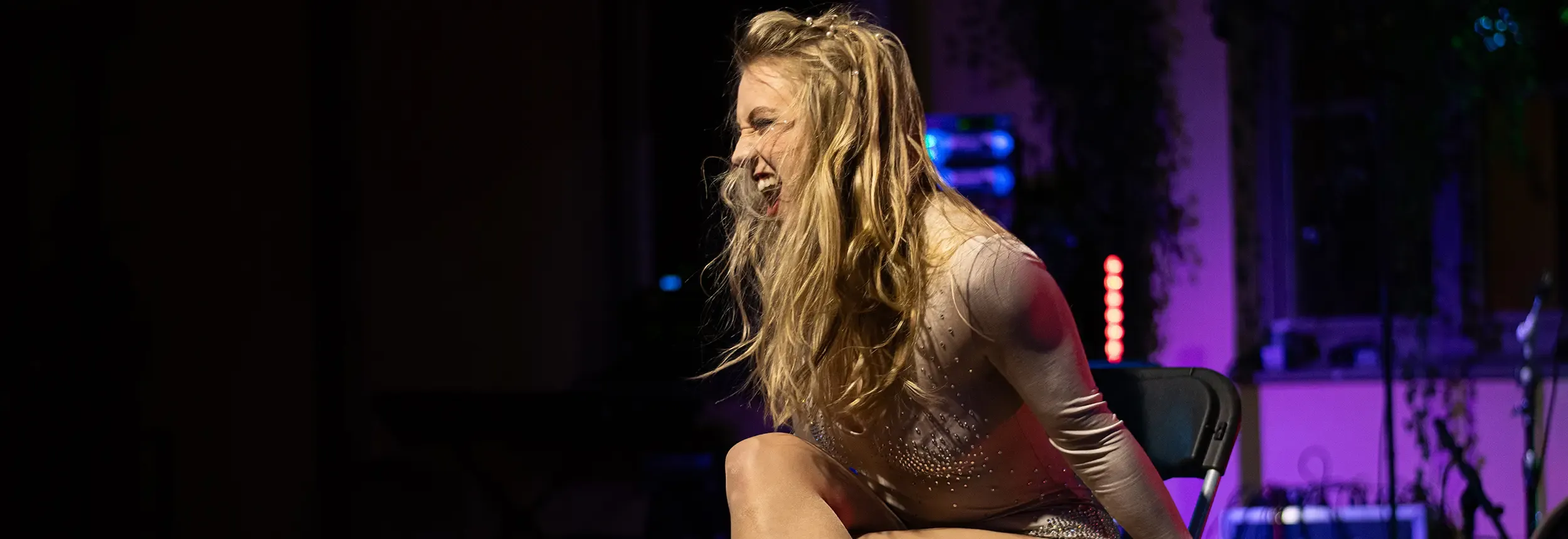 Showartist sitter på stol i ett uttrycksfullt scenmoment med stark närvaro och dramatisk ljussättning.