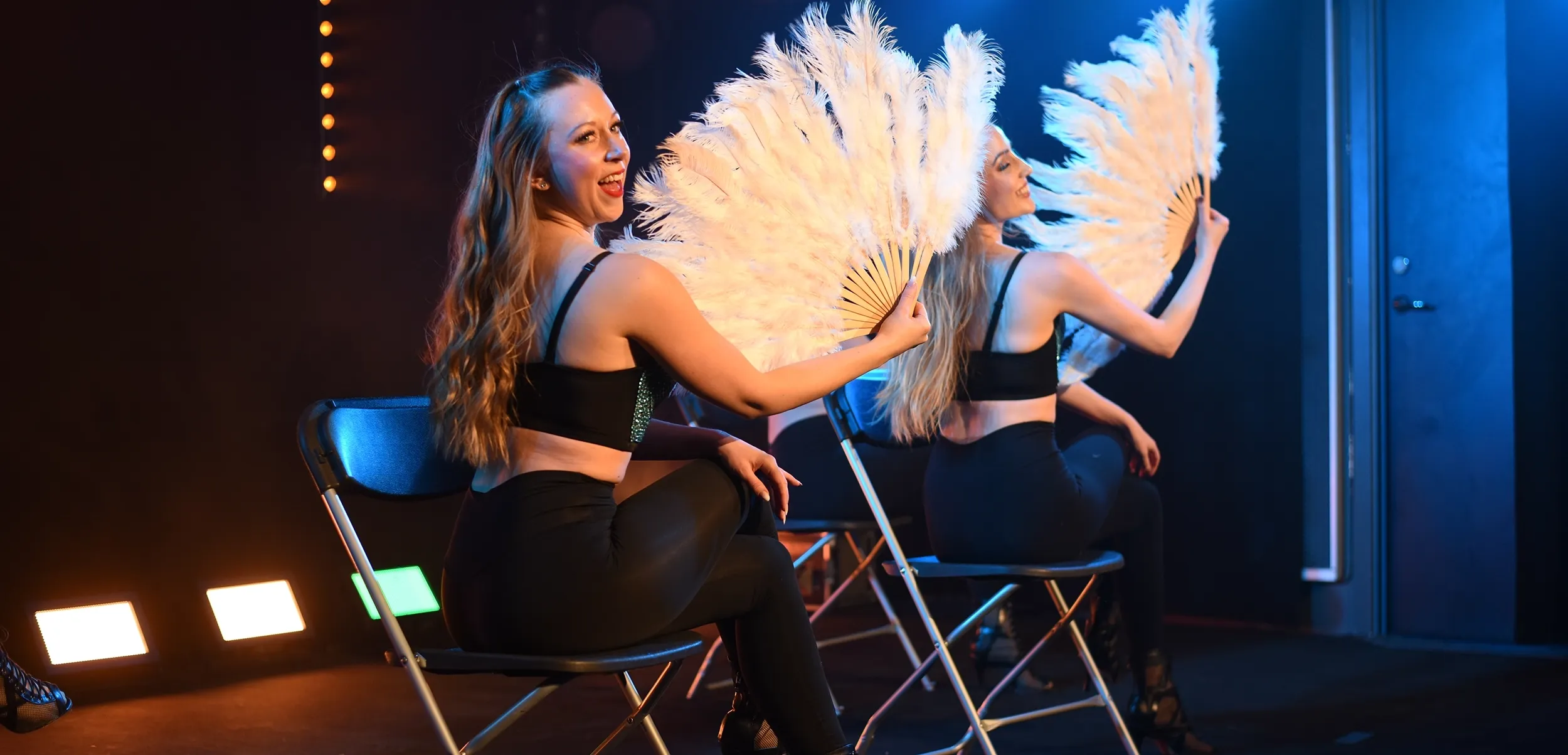 Två showartister uppträder med fjäderfantasier i en elegant och lekfull scenkoreografi.